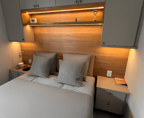 quarto planejado com portas no beige e painel da cama amadeirado com iluminação em led instalado pela DECORATA em Praia Grande