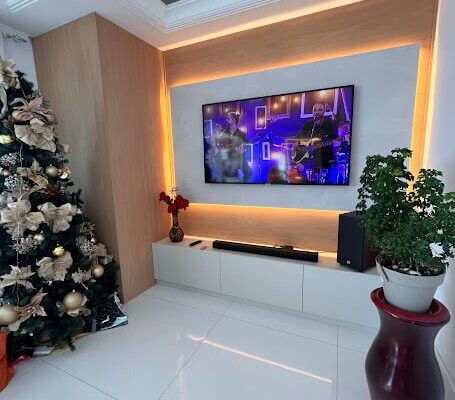 Painel de TV Amadeirado com iluminação indireta e rack branco diamante instalado pela DECORATA no Bairro da Aviação em Praia Grande