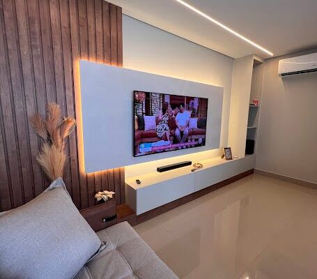 Painel de TV com ripado amadeirado e rack Off White com iluminação indireta instalado pela DECORATA na Vila Tupi em Praia Grande