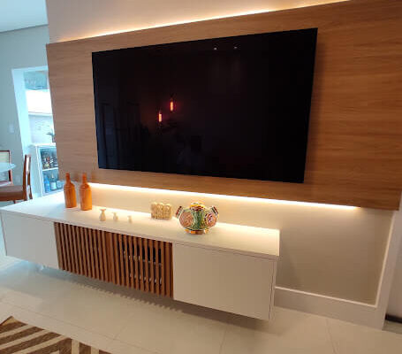 Painel de TV com portas ripadas e iluminação indireta do painel amadeirado, projeto instalado no Itararé em São Vicente pela DECORATA